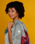 Curly haired woman wearing denim jacket with Courage is found in unlikely places enamel pin