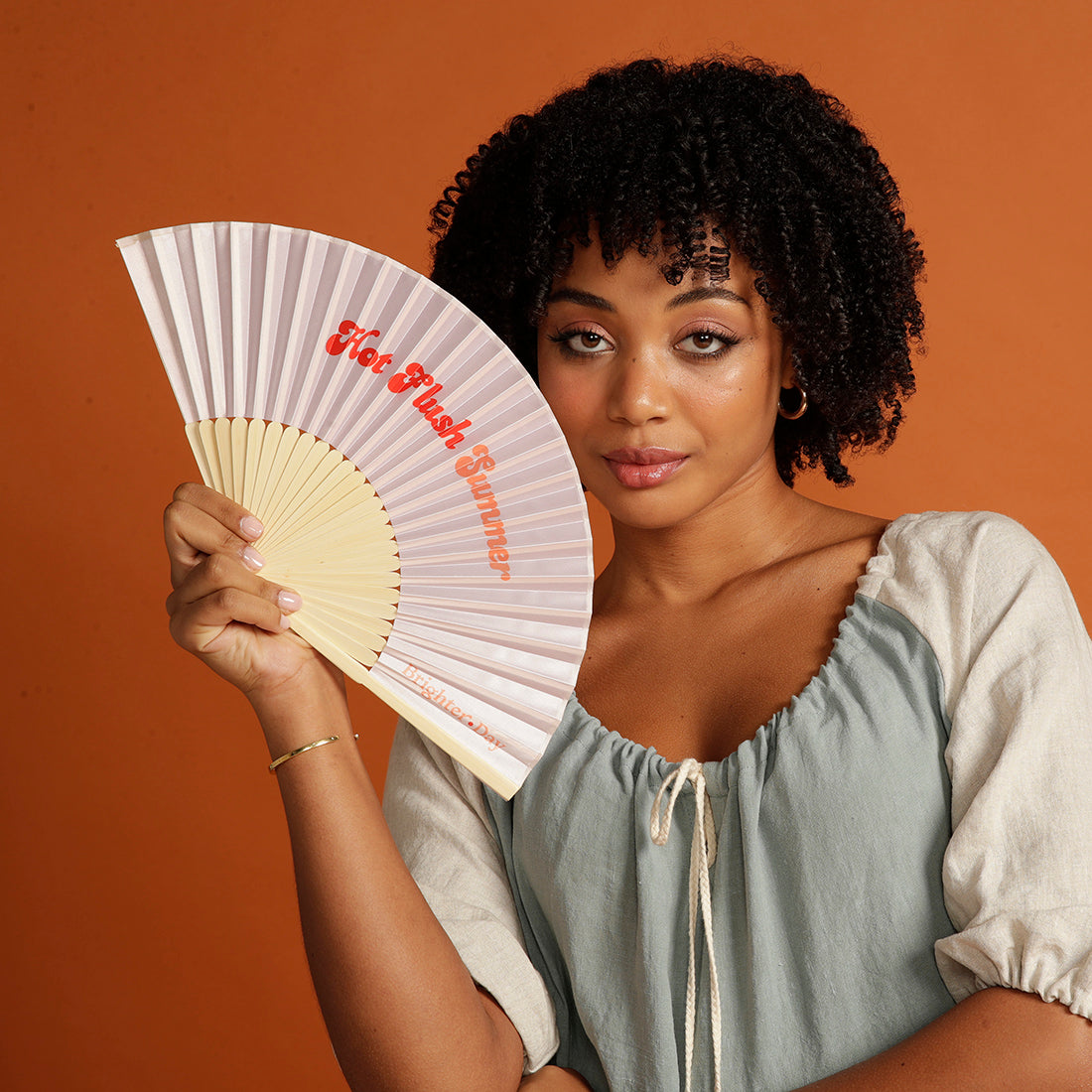 Curly haired woman holding pink Hot Flush Summer Fan too her face