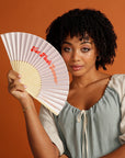 Curly haired woman holding pink Hot Flush Summer Fan too her face