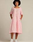 brown woman with black hair is wearing a linen dress that is light pink, she has her hands in the pockets