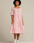 brown woman wears a light pink linen dress with white shoes