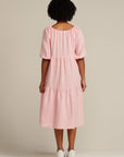 woman with black curly hair facing her back to camera is wearing a pink linen dress that is below knee length