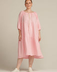 white woman facing the camera wearing a pink linen dress and white shoes