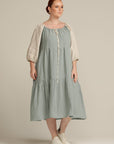 woman wearing a sage green and natural sleeve linen dress and white shoes
