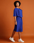 Curly haired woman wears royal blue dress with ruffle sleeve detail