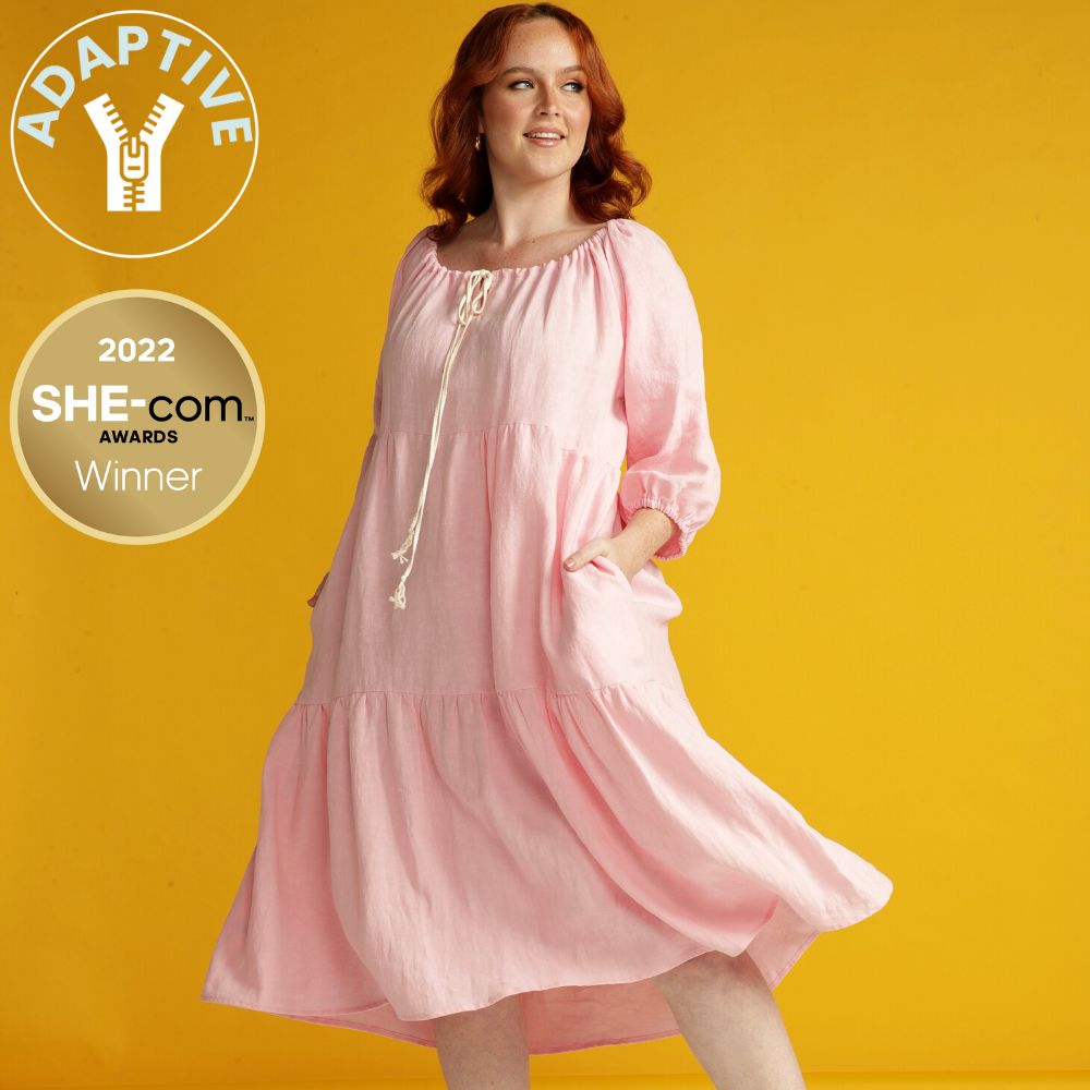 woman with red hair wearing a pink linen adaptive linen dress. Adaptive icon and SHEcom award winner icon feature on the left