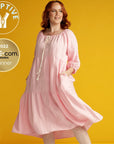 woman with red hair wearing a pink linen adaptive linen dress. Adaptive icon and SHEcom award winner icon feature on the left