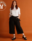 woman wearing black culottes and white tee standing with orange background