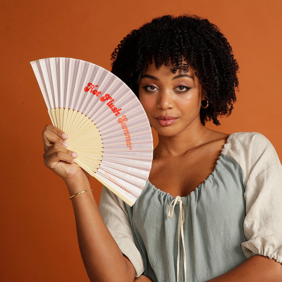 Curly haired woman holding pink Hot Flush Summer Fan too her face