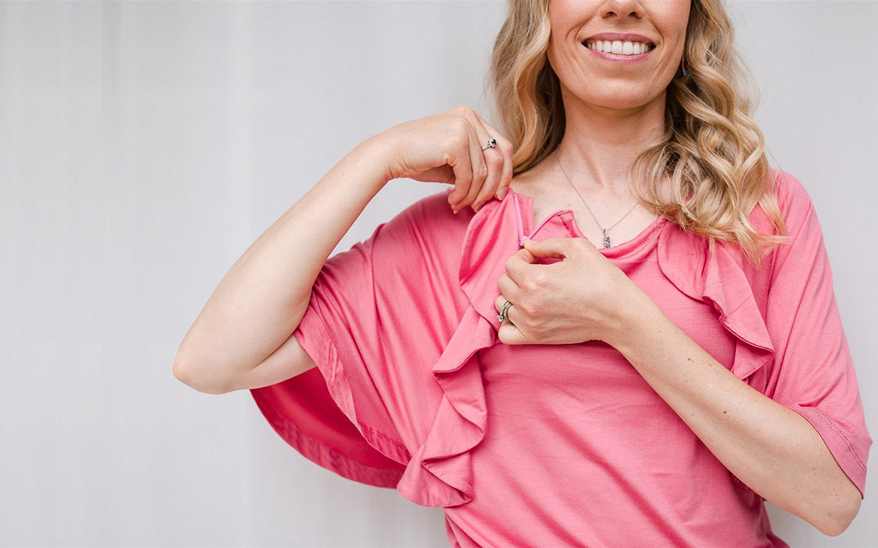 a woman wearing an adaptive pink ruffle top, undoing a zip on the left of the chest