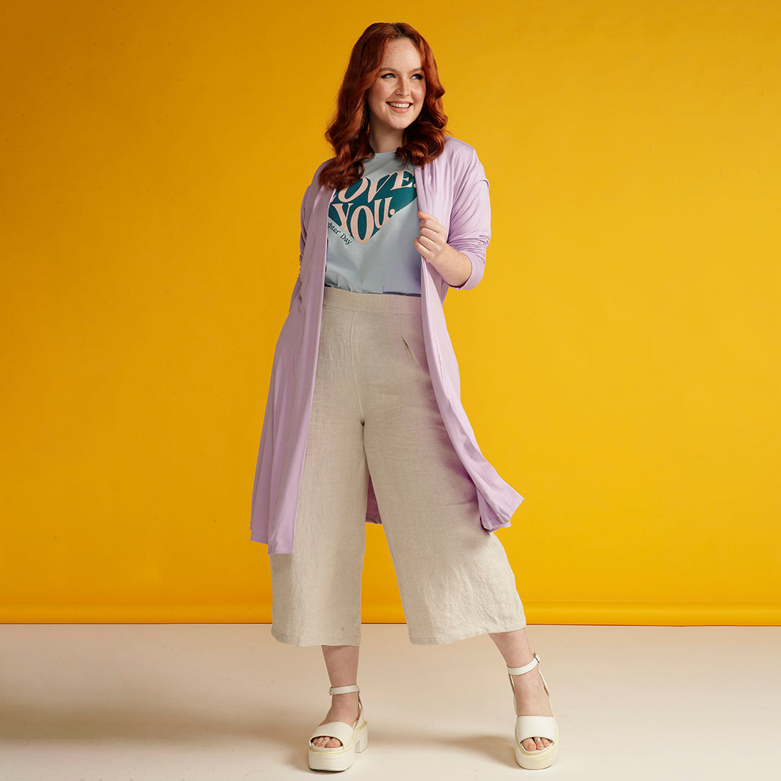Red haired woman wears lilac cardigan and beige linen culottes
