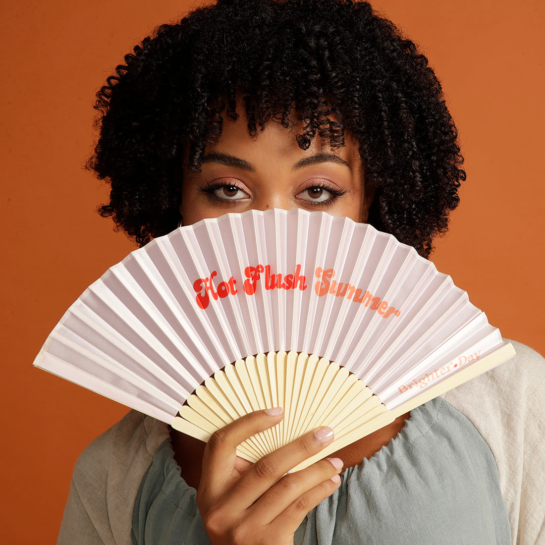 Curly haired woman holding pink Hot Flush Summer Fan over her face