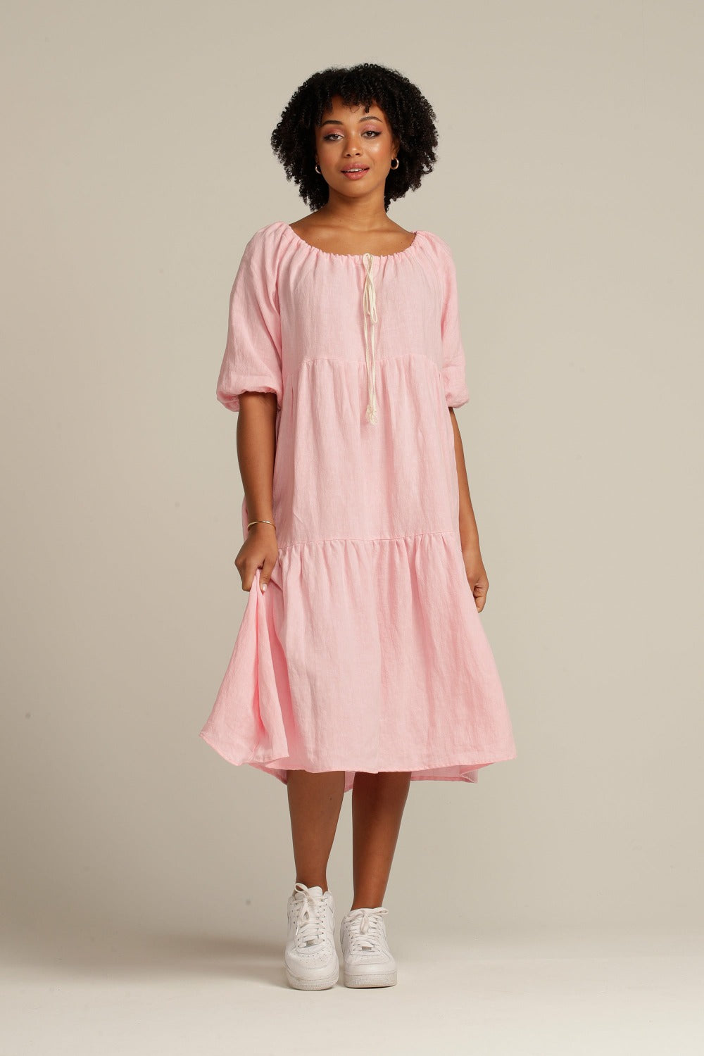 brown woman wears a light pink linen dress with white shoes