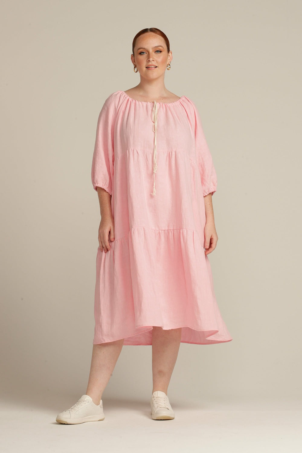 white woman facing the camera wearing a pink linen dress and white shoes