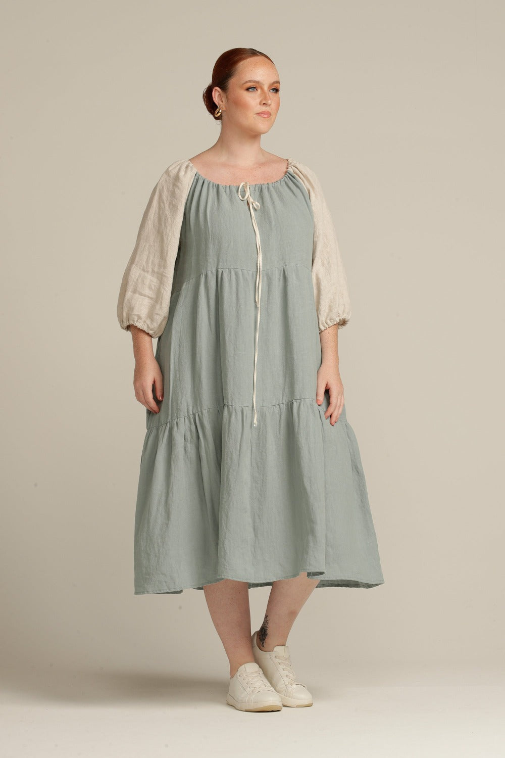woman wearing a sage green and natural sleeve linen dress and white shoes