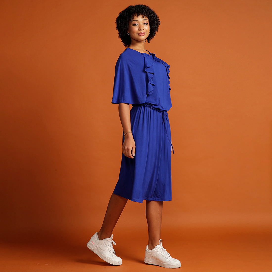 Curly haired woman wears royal blue dress with ruffle sleeve detail