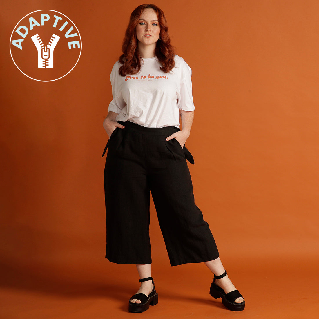woman wearing black culottes and white tee standing with orange background