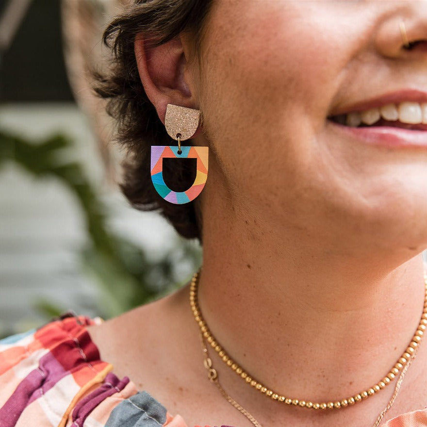 woman wearing earrings with sparkly gold top and rainbow colourful dangle shape